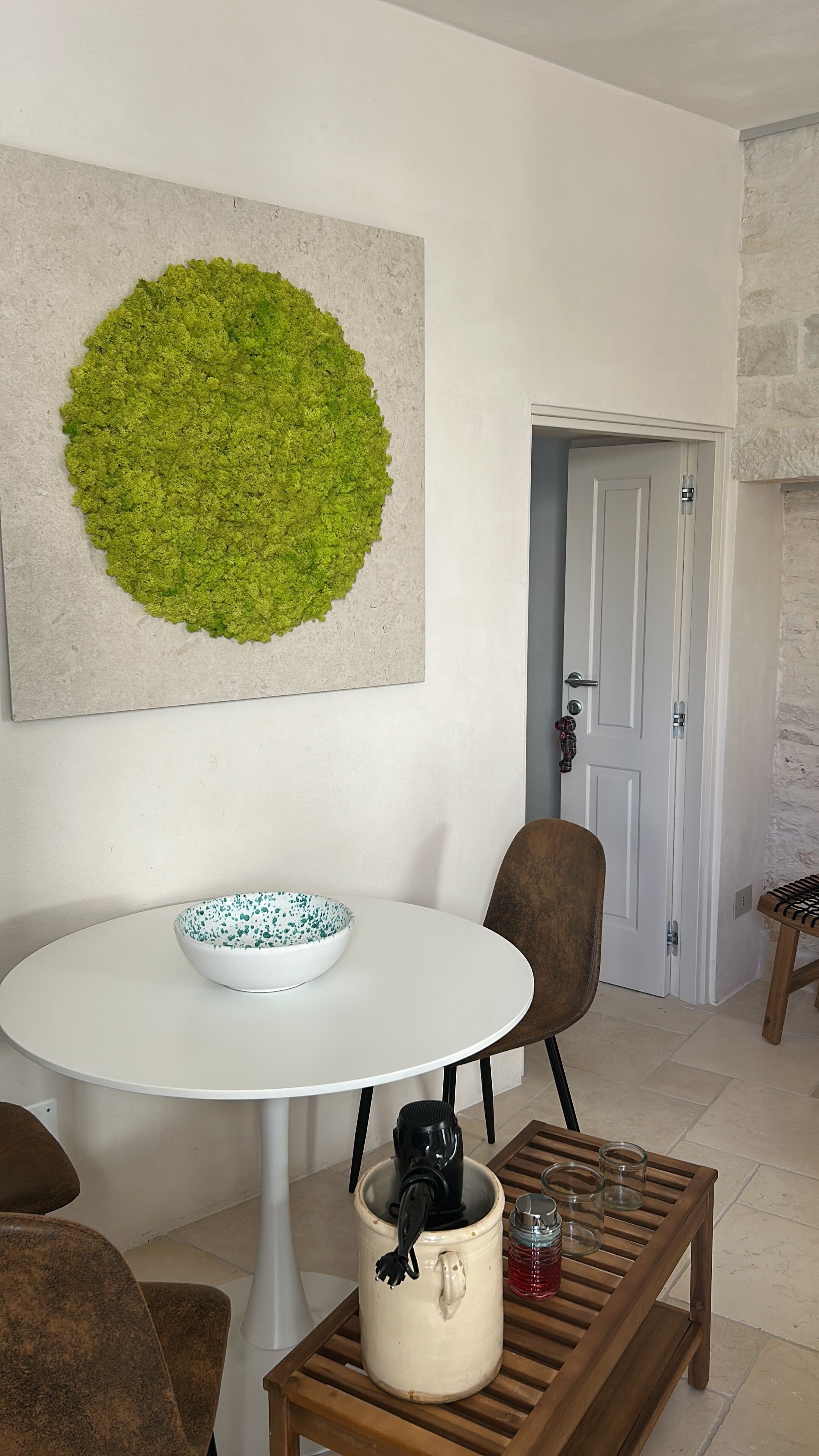 A dining area with a round white table, a bowl, a mug, and a coffee maker. There is a door in the background and a textured wall.