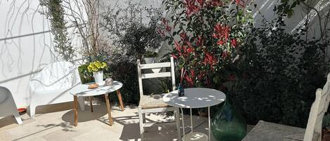 Un patio con una mesa blanca, dos sillas blancas y una mesa redonda pequeña con un jarrón de flores amarillas.