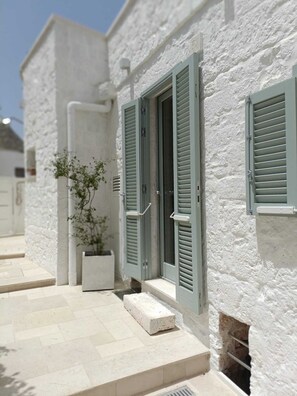 A white building with green shutters, a potted plant, and a tiled entrance. - Montesanto 60 Suite & Relax Alberobello (Alberobello)