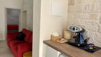 A compact kitchen with a coffee machine, a wooden side table, and a red sofa in the adjacent living area.