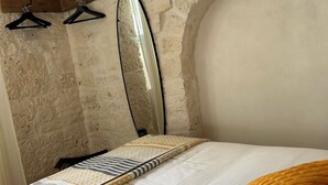 A bedroom with a bed, a hanging mirror, and two black hangers on a textured wall. - Montesanto 60 Suite & Relax Alberobello (Alberobello)