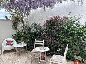 A small outdoor seating area with a white table and chairs, surrounded by various plants and a white wall. - Montesanto 60 Suite & Relax Alberobello (Alberobello)