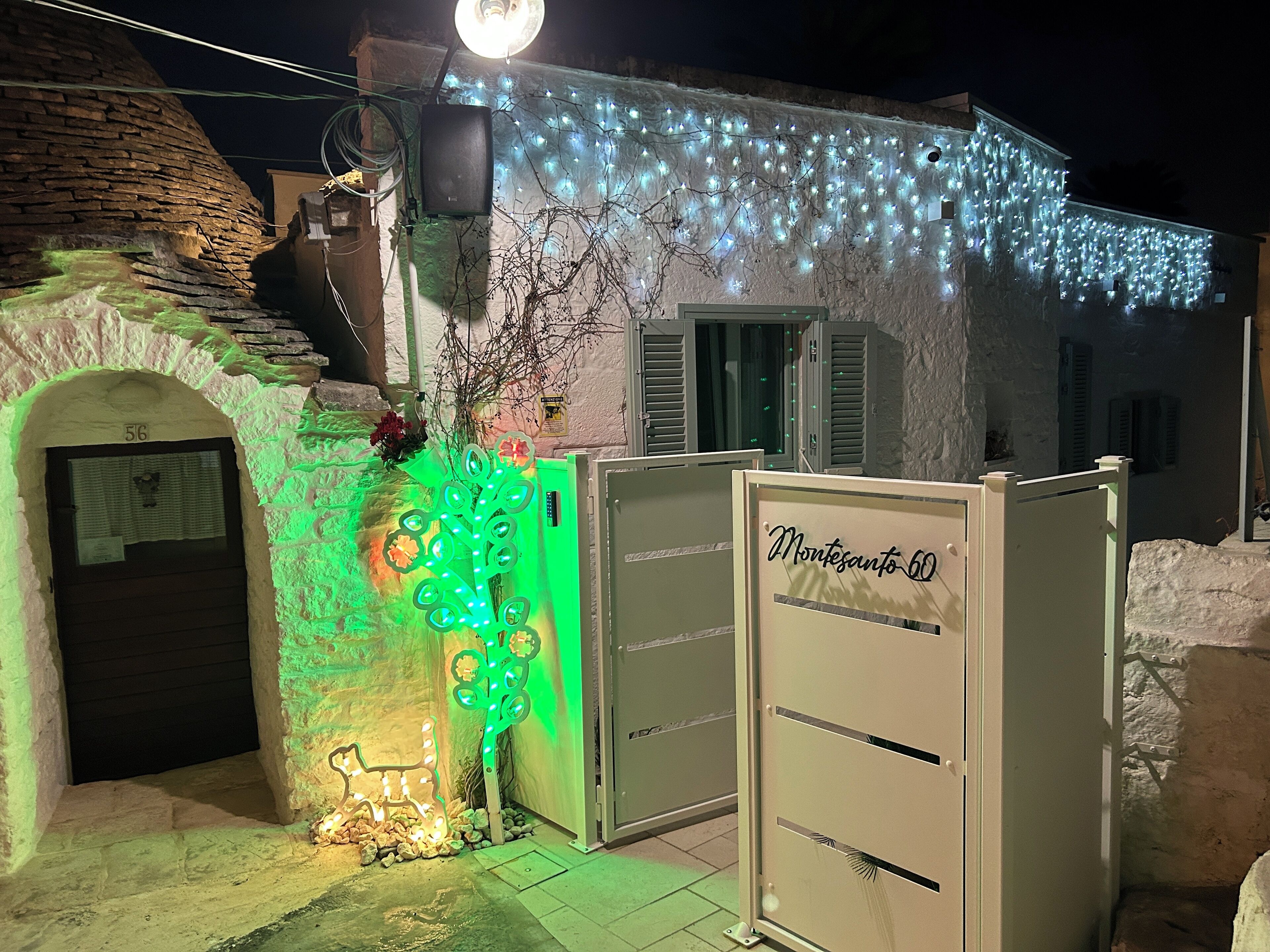 Un edificio con fachada de piedra, decoración de árbol iluminada en verde y un cartel que dice "Montesanto 60".
