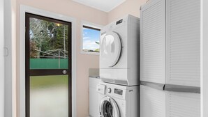 Een wasserette met gestapelde wasmachines en drogers, een deur met uitzicht op een groen buitengebied, en een klein raam.