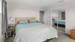 Een slaapkamer met een bed, nachtkastjes, een spiegel en een kledingkast.