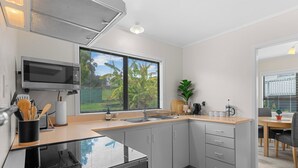 Een moderne keuken met grijze kastjes, een magnetron en een groot raam met zonwering.