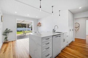 A modern kitchen with white cabinetry, a marble island, and pendant lighting. - The Olive Corner- Martinborough Holiday Home (Martinborough)