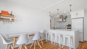 Et moderne køkken med en central ø, barstole og et spiseområde med et glasbord og stole.