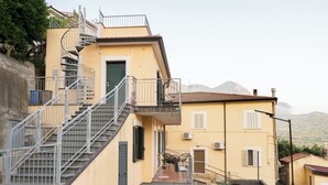 A yellow building with a spiral staircase leading to a balcony. There is a small outdoor seating area with a table and chairs. - Panoramic house surrounded by nature just 8 minutes from the beaches of Diamante (Maiera')