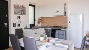 A modern kitchen with white cabinets, a built-in stove, and a refrigerator. There is a dining table with chairs and a small potted plant on the table. - Panoramic house surrounded by nature just 8 minutes from the beaches of Diamante (Maiera')