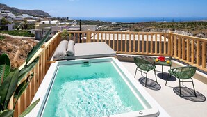 A hot tub with a view of the sea, wooden deck, and outdoor seating area.