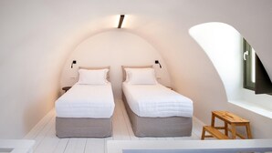 A compact, two-bed room with a sloped ceiling, a small wooden bench, and a window with a view of the outside.