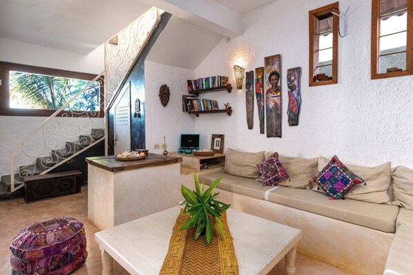 Una sala de estar con una escalera, un sofá, una mesa de centro con una planta y una estantería llena de libros y objetos decorativos.