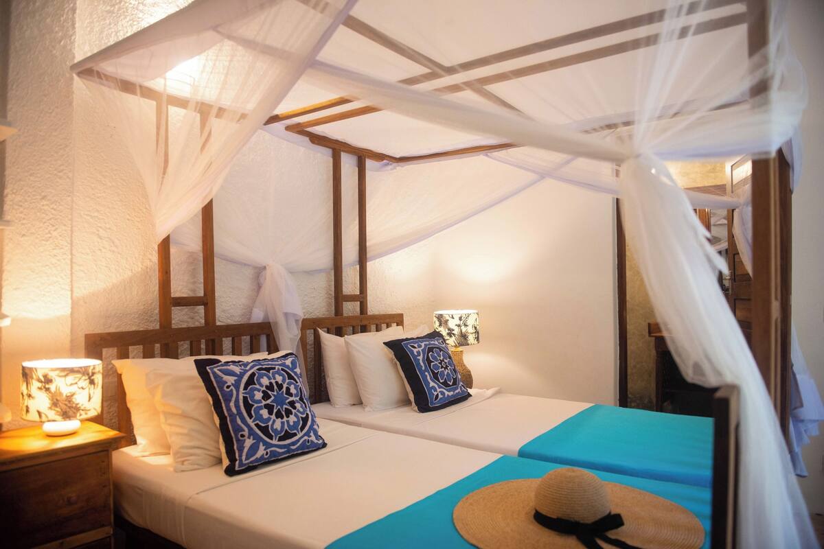A room with a bed under a canopy, bedside lamps, and a hat on the bed.