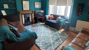 A living room with a fireplace, a sofa set, a coffee table, and a large window with blinds. - Stylish home with garden . Located near pubs, parks beach and town. (Brighton and Hove)