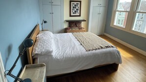 A bedroom with a bed, a desk, a chair, a lamp, and a window with a view of buildings. - Stylish home with garden . Located near pubs, parks beach and town. (Brighton and Hove)