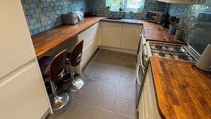 A modern kitchen with white cabinets, a wooden countertop, a gas stove, and a window providing natural light. - Stylish home with garden . Located near pubs, parks beach and town. (Brighton and Hove)