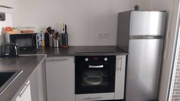 A compact kitchen with a built-in oven, a microwave, a toaster, and a refrigerator.