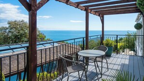 A wooden deck with a view of the ocean, a pool, and outdoor seating.