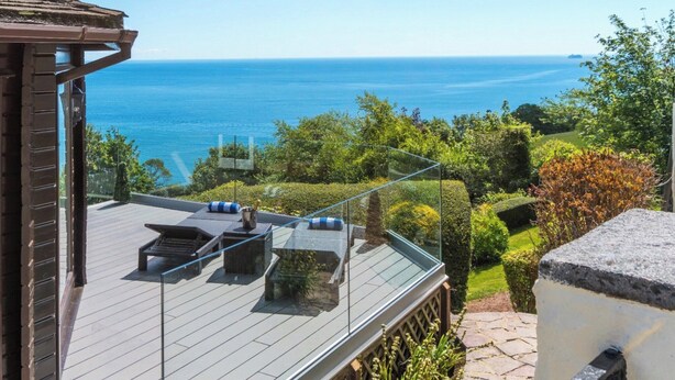 A balcony with a clear view of the sea, a wooden deck, and a glass railing.
