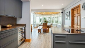 A modern kitchen with grey cabinets, a wooden dining table, and a large window overlooking greenery.
