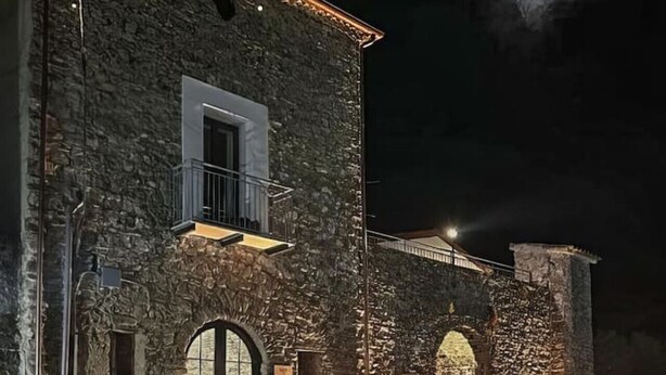 A stone building with a balcony and a large arched doorway, illuminated by exterior lighting. - Casa Vacanze Signora Cinzia (Torchiara)