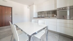 A modern kitchen with white cabinets, a stainless steel oven, and a white dining table with chairs. - Casa Vacanze Signora Cinzia (Torchiara)