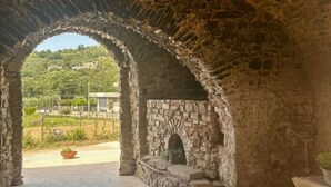An arched stone structure with a brick floor, a fireplace, and a view of a green landscape. - Casa Vacanze Signora Cinzia (Torchiara)