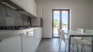 A modern kitchen with white cabinets, a stainless steel range hood, and a dining area with a glass table and white chairs. - Casa Vacanze Signora Cinzia (Torchiara)