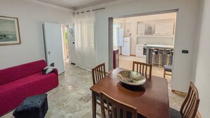 Un coin repas avec une table et des chaises en bois, un canapé rouge et une cuisine en arrière-plan.