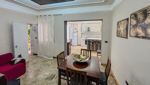 Un espace repas comprenant une table et des chaises en bois, un canapé rouge et un plafond doté d’un éclairage encastré.