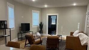 Una sala de estar moderna con comedor, piso de madera y un televisor grande.
