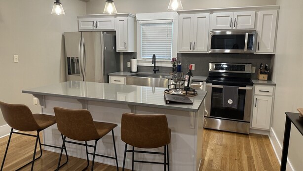 Una cocina moderna con armarios blancos, electrodomésticos de acero inoxidable y una isla central con taburetes de bar.