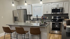 Una cocina moderna con armarios blancos, electrodomésticos de acero inoxidable y una isla de madera con taburetes de bar.