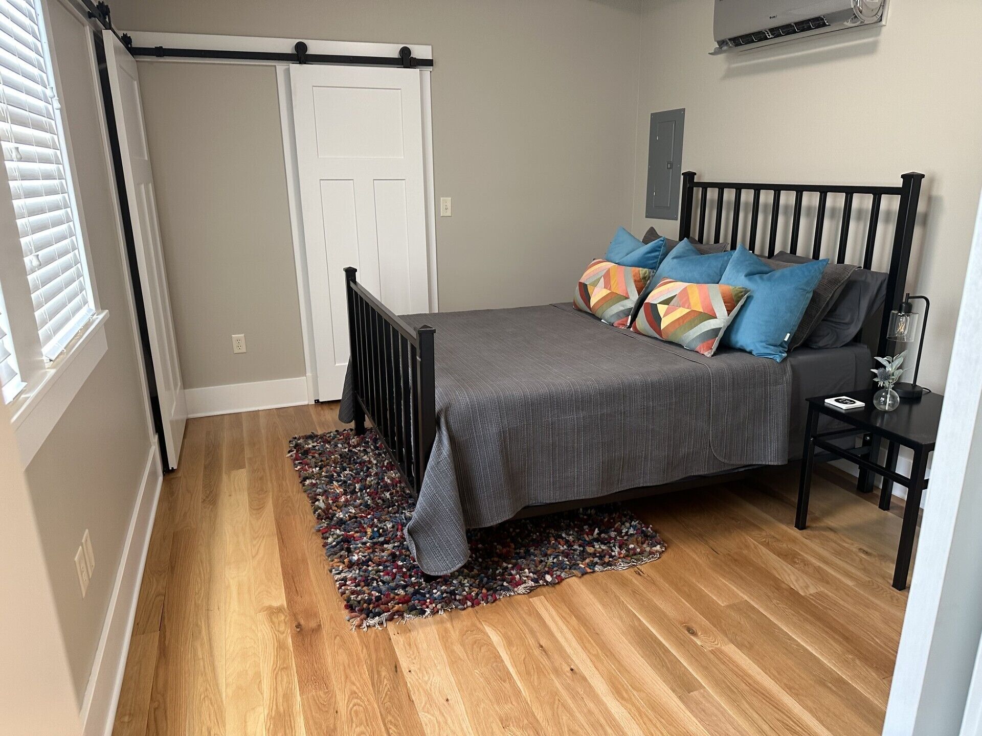 A bedroom with a bed, a black metal headboard, a small bedside table with a lamp, and a colorful rug.