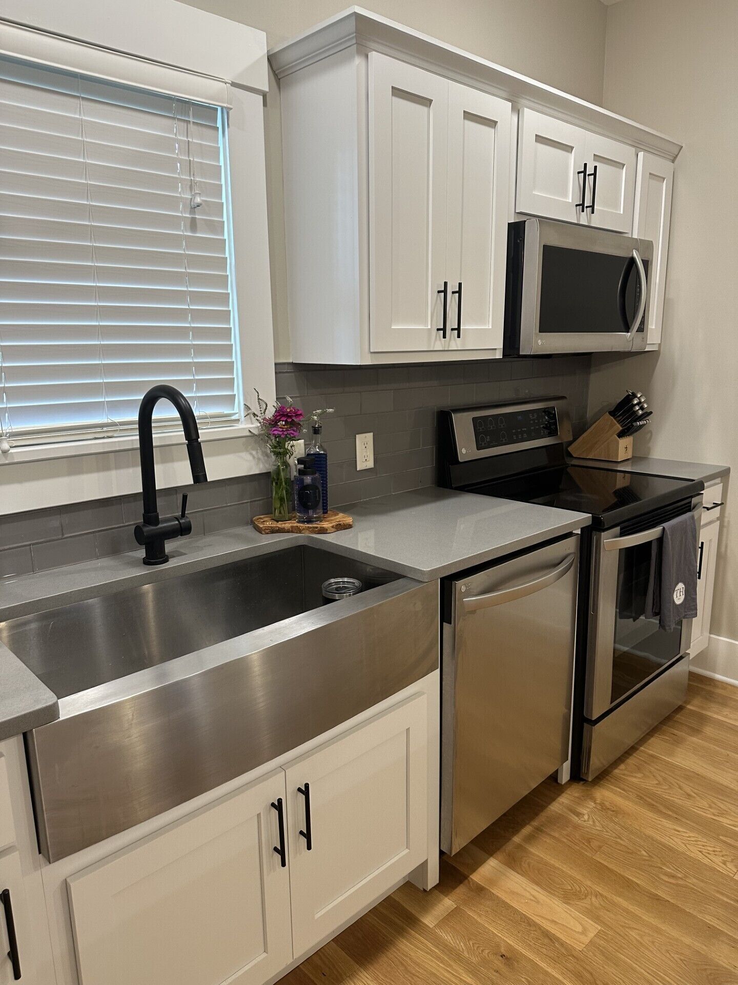 A modern kitchen with stainless steel appliances, white cabinetry, and a window with blinds.