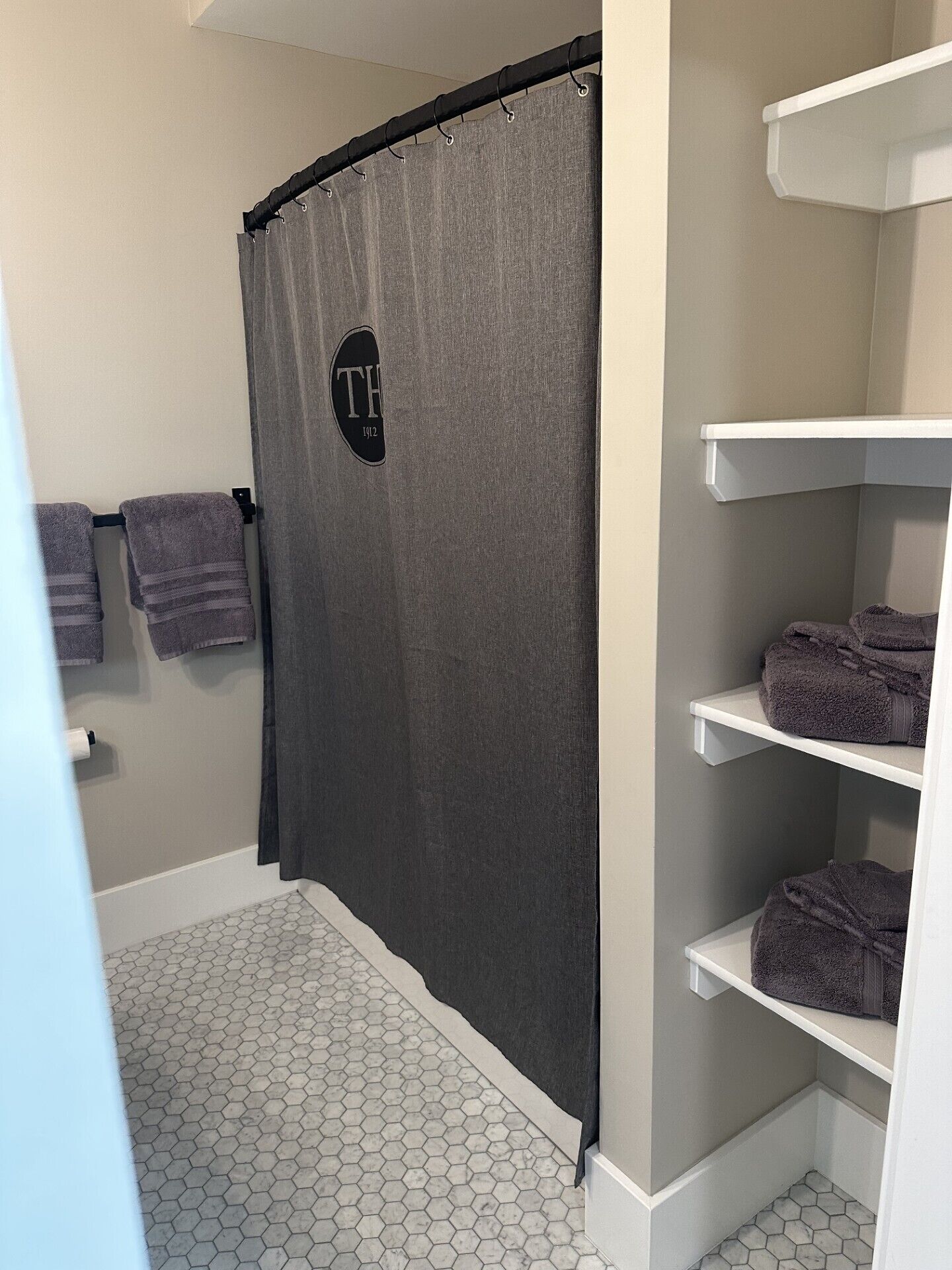 Un baño con cortina de ducha, toallas y estantes.