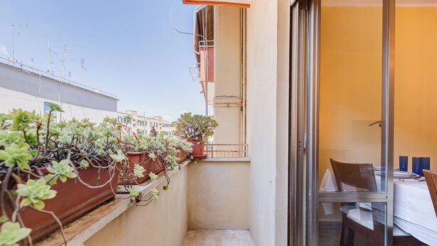 A narrow balcony with potted plants and a glass door leading to a dining area with a table and chairs. - The Popes' Oasis - 2 steps from Trastevere and Historical Center (Roma)