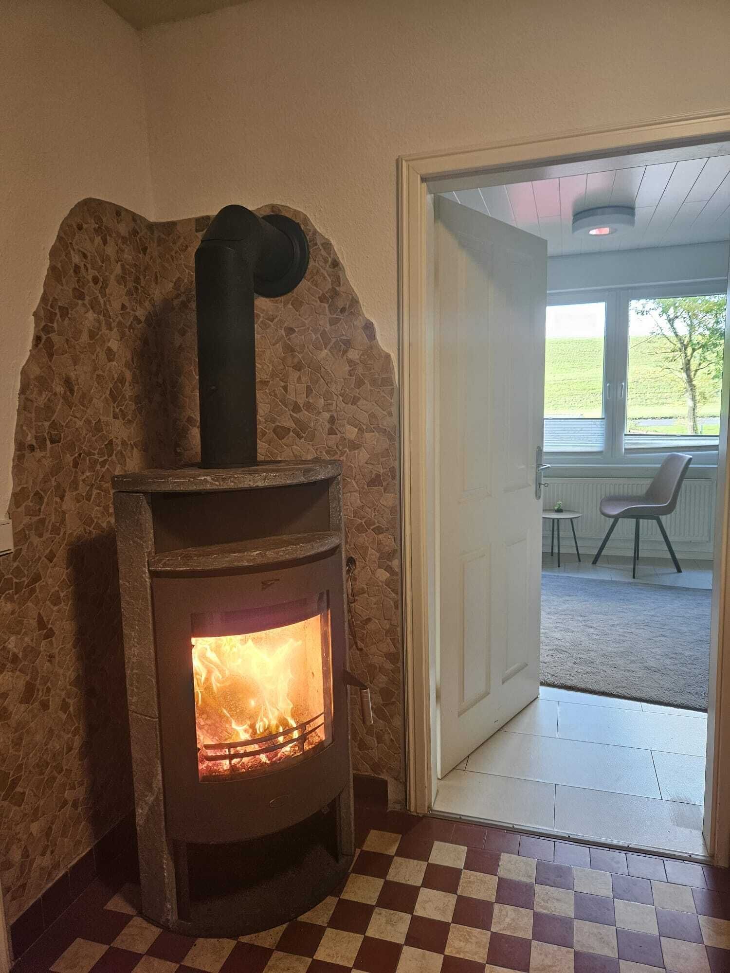 Eine Steinsäule mit Kaminofen, kariertem Boden und einer Tür zu einem Außenbereich mit Sitzgelegenheiten.