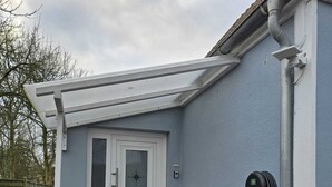 Une maison avec une porte blanche, un petit porche et un panneau solaire fixé au mur.