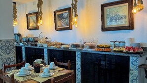 Een eetgedeelte met een tafel voor vier personen, een buffet met verschillende soorten eten, en twee ingelijste schilderijen aan de muur.