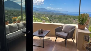 A balcony with a sofa and chair, a small table, and potted plants. - Detached comfortable stone house with wonderful views 10 min from the sea (Kardamyli)