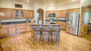 Una cocina con armarios de madera, un refrigerador de acero inoxidable y una isla central con taburetes de bar.