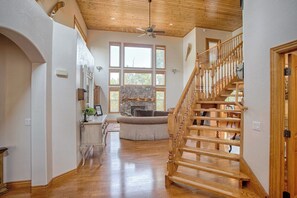 A spacious hallway with a wooden staircase, a stone fireplace, and large windows.