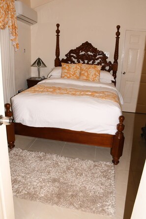A bedroom with a wooden four-poster bed, white bedding, and a floral-patterned throw.