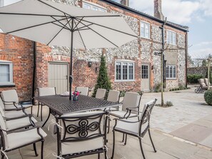 Un espace patio avec une table et des chaises, un grand parasol, et un bâtiment en briques doté de fenêtres et d’une porte.