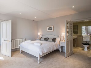 Une chambre à coucher avec un lit, deux tables de chevet, un radiateur, une porte et une salle de bain visible à travers une porte ouverte.