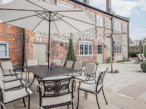 A patio area with a table and chairs, a large umbrella, and a brick building with windows and a door.