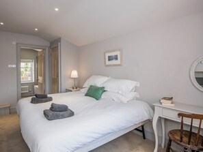 A bedroom with a bed, bedside lamp, a small table with a chair, a mirror, and a framed picture on the wall.
