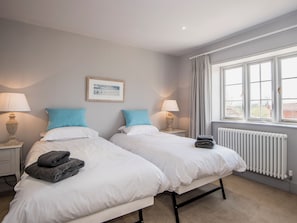 A hotel room with two beds, a framed picture on the wall, a window with curtains, and a radiator. - This stunning property is a real treat for history lovers. (Syderstone, near Fakenham)